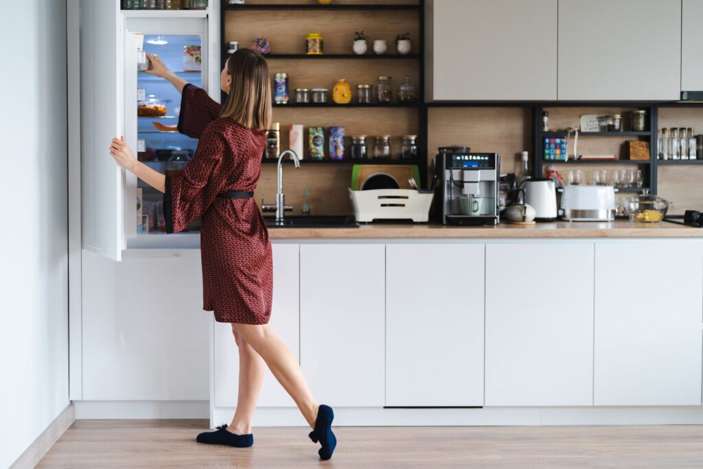 Woman using sponge and natural cleaner to scrub refrigerator interior walls.