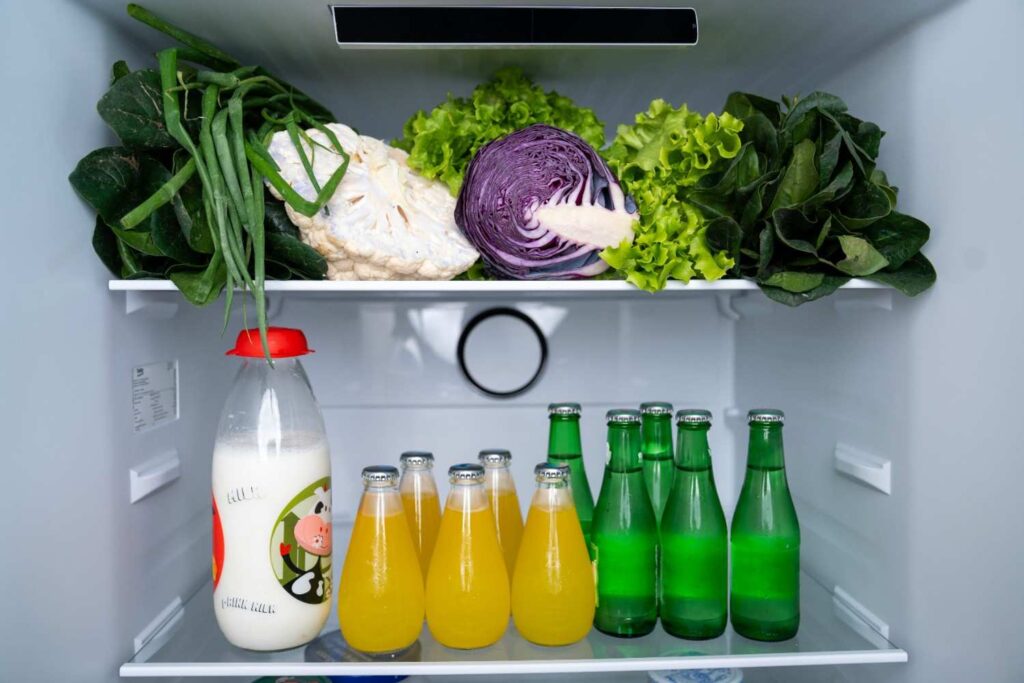 Woman cleaning refrigerator shelves with eco-friendly cleaner and cloth, demonstrating natural fridge cleaning.
